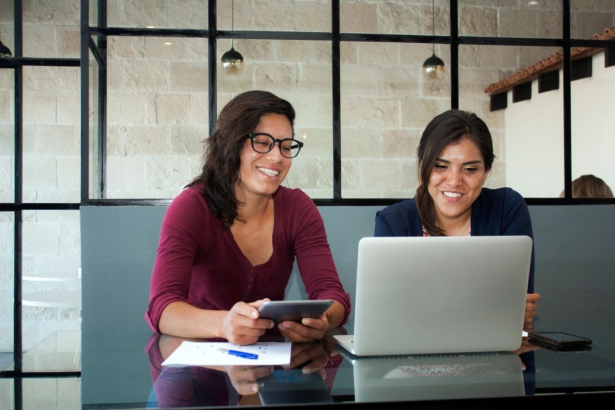 Two women smiling using laptop and tablet